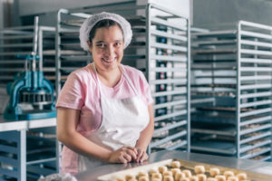 Kvinne i bakeri med rader av bakst på et brett